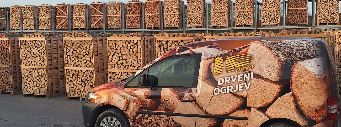 Dostavno vozilo IP-DRVO pred složenim sanducima ogrjevnog drva