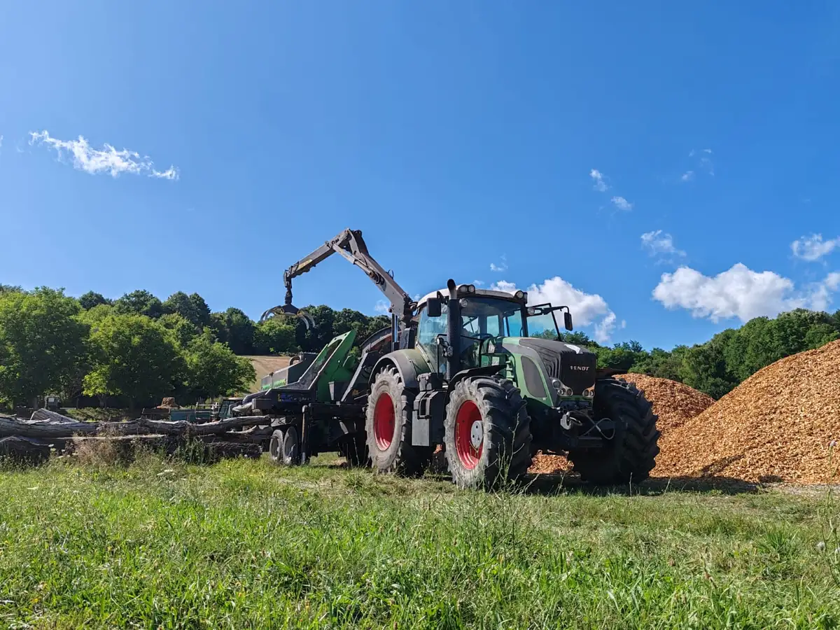 Traktor s priključnom sječkalicom drobi drvo u sječku pored velike hrpe gotove sječke